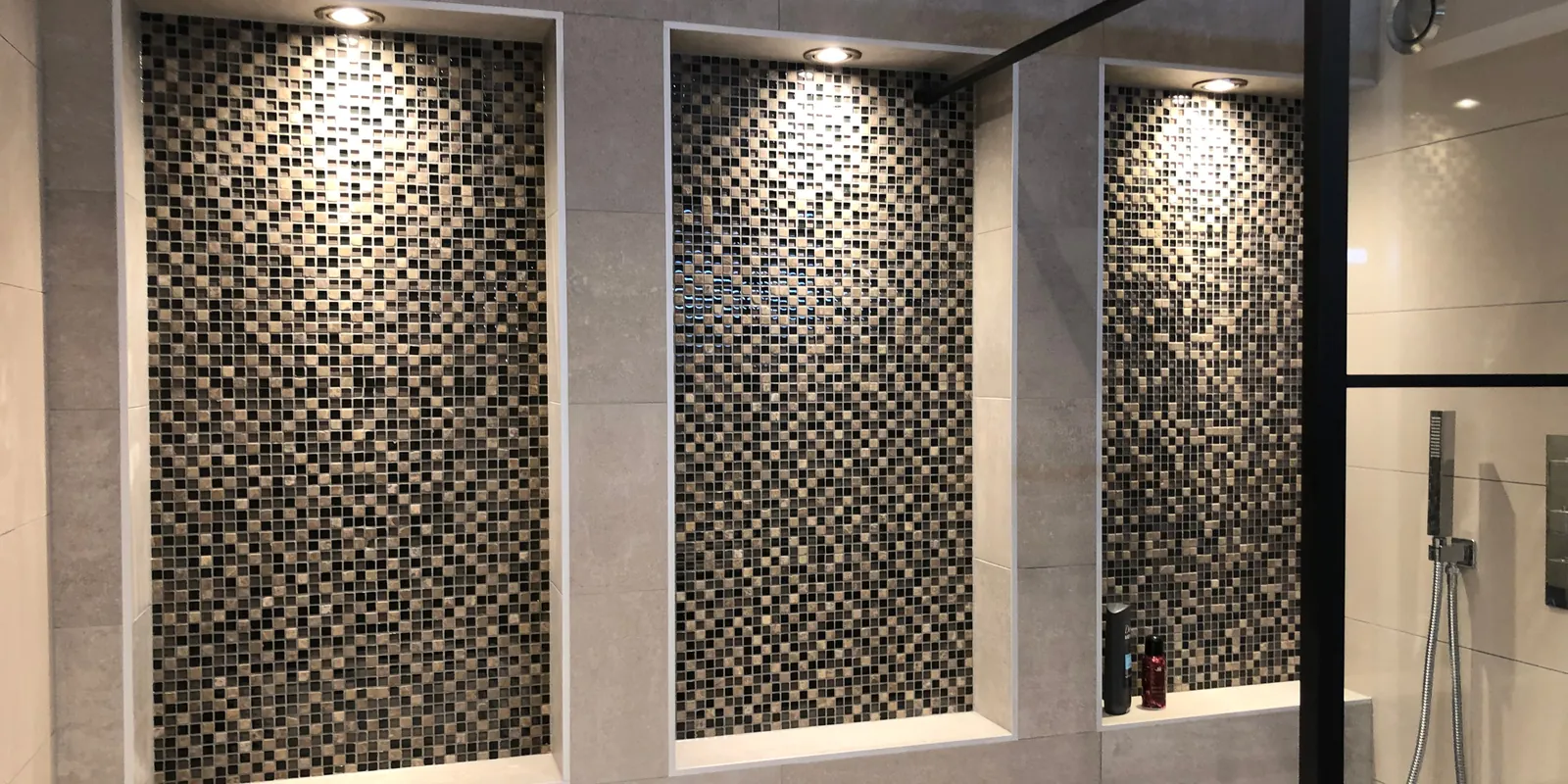 Badkamer met drie verlichte mozaïeknissen en zwart omlijste douche