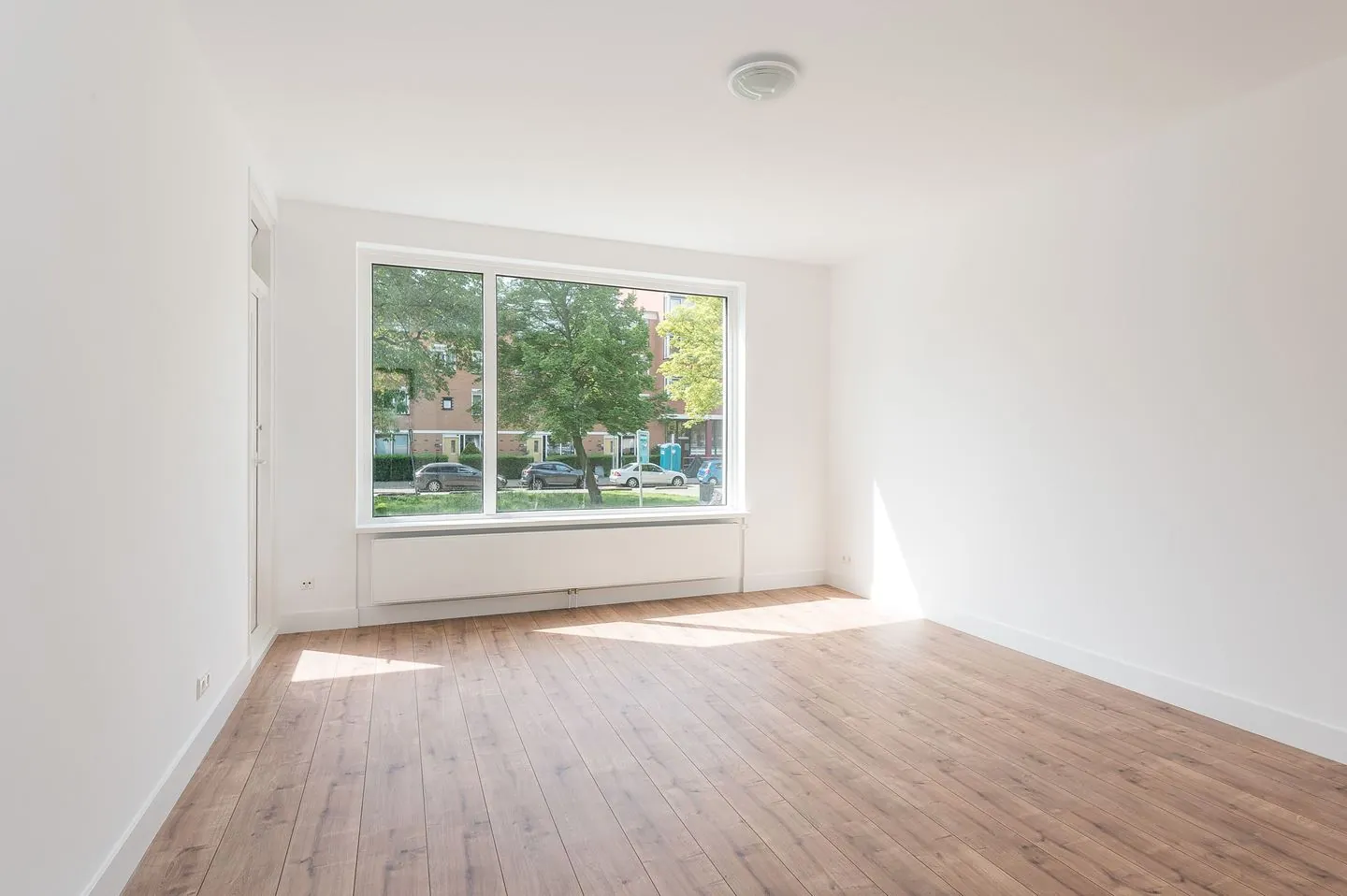 Gerenoveerde lichte woonkamer met groot raam en lichte eiken vloer